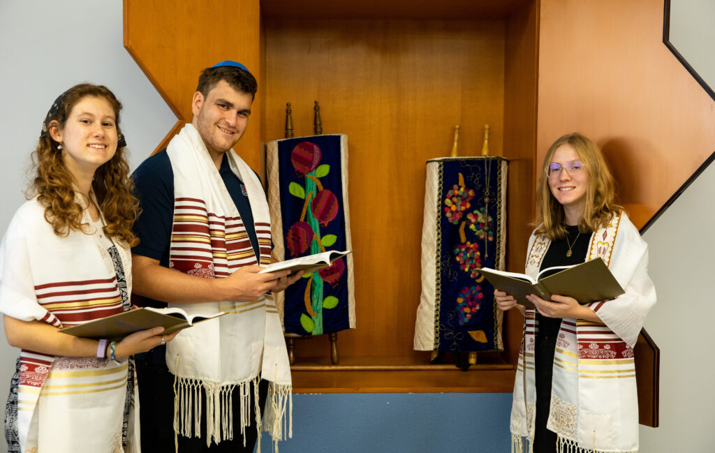 Three students stand around two Torah scrolls